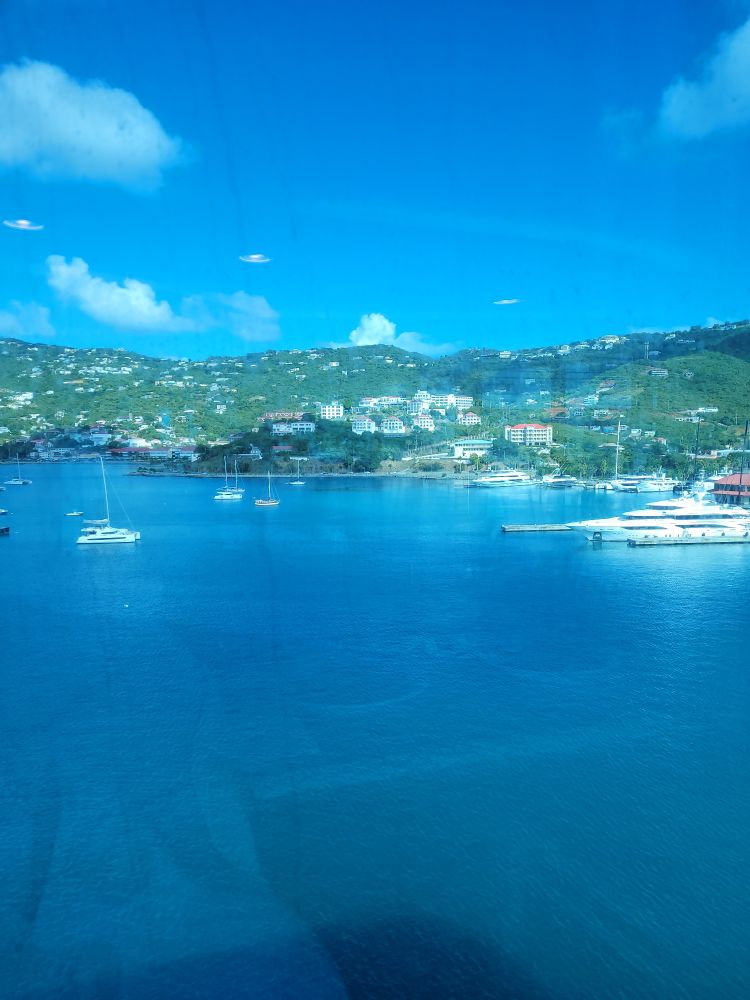 A view of the harbor in St. Thomas. The sky and the water are both a beautiful shade of blue and the green mountains and hills are dotted with houses and hotels. 