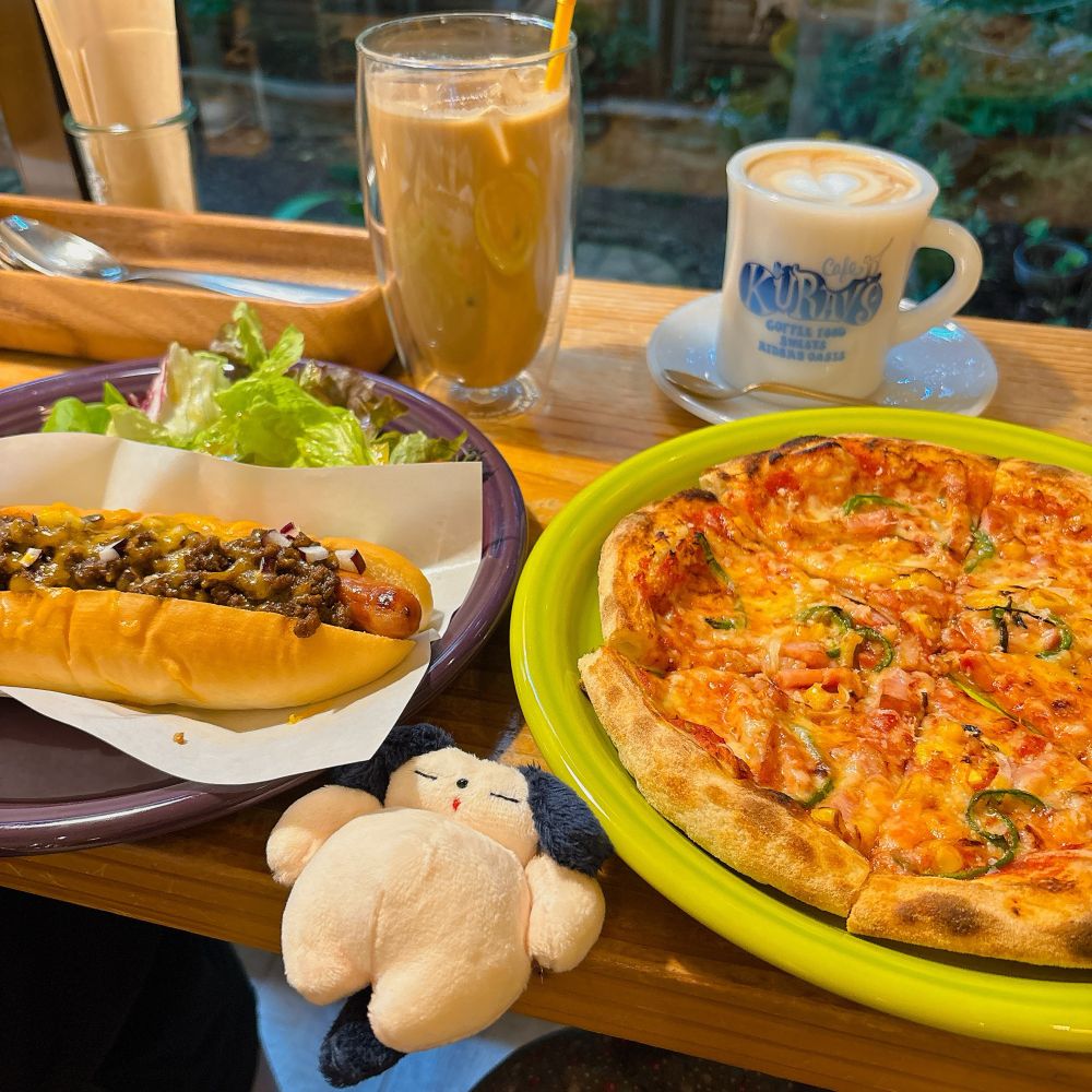 カフェのテーブルの写真。ミックスピザとチリドッグ。カフェオレのホットとアイスが一つずつ。ふっくらとしたお腹のわんちゃんのぬいぐるみを添えて。