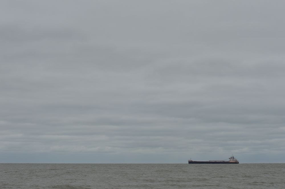 a photo of a ship sailing across a lake under an overcast sky - gray between grays