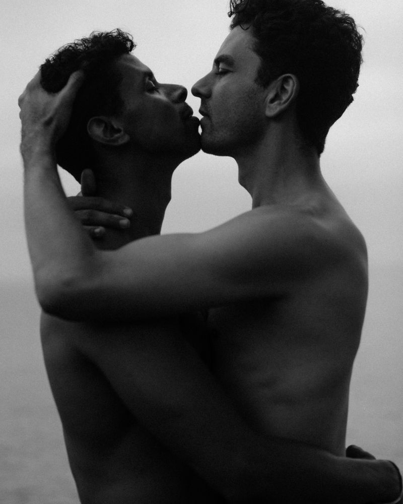 black and white photo of two men embracing and kissing on fire island, in the fog. 