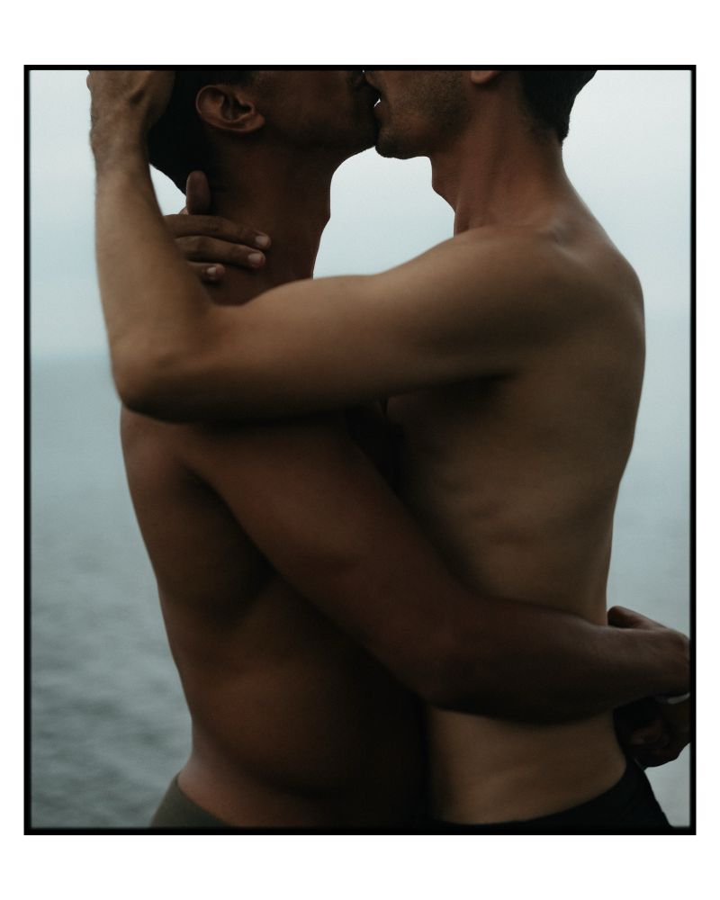 black and white photo of two men embracing and kissing on fire island, in the fog. 