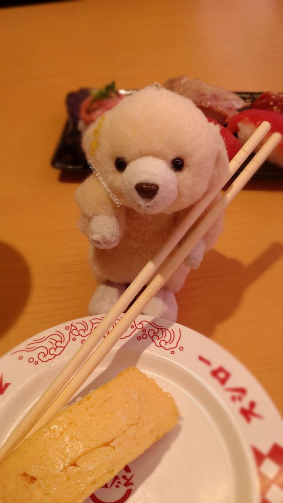 箸を持ってたまごのお寿司を食べようとするクマのぬいぐるみ