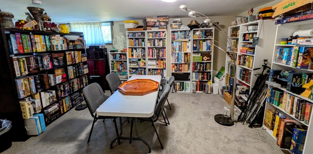 A room full of board games, with a table in the middle with a Crokinole board in the middle.