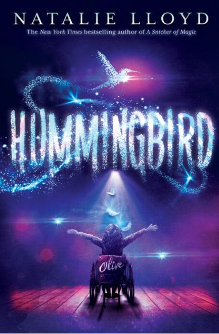 Book cover title Hummingbird by Natalie Lloyd. Girl in a wheelchair at center stage facing the spotlight. Back of the wheelchair says the name Olive.