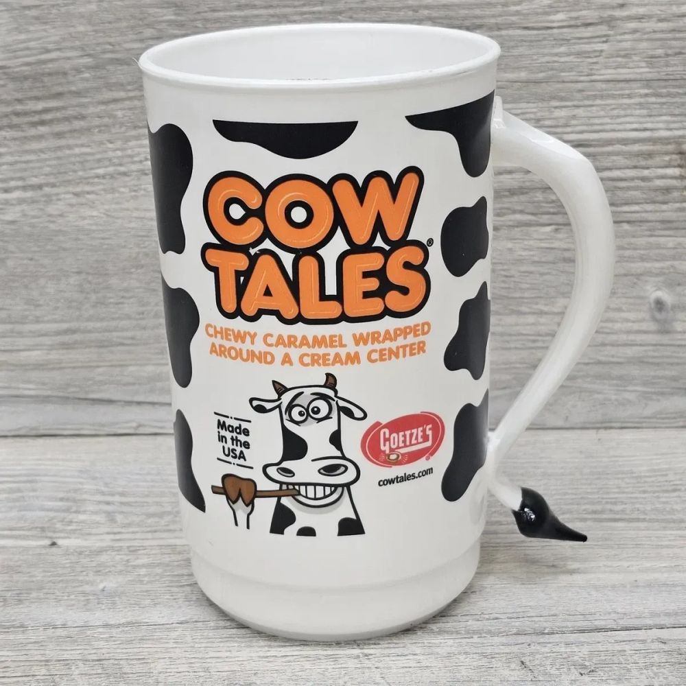 Ceramic promotional mug for Cow Tales chewy caramels with cream center. Mug is white with black cow spots and orange logo.