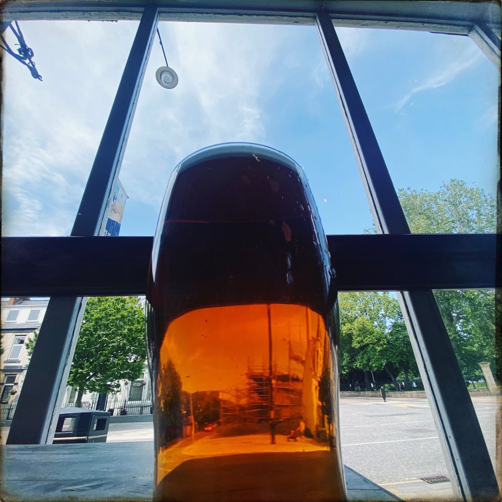 Glass of Bass Ale photographed at at dramatic angle, with a streetscape beyond the windowpanes 