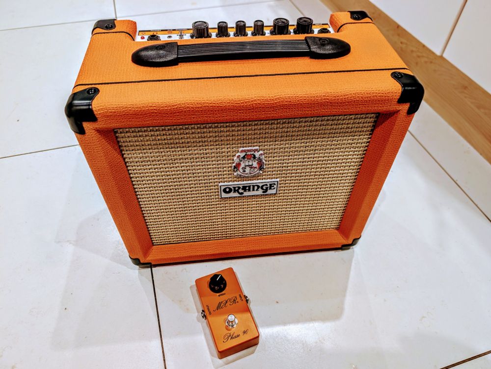 An Orange Crush 20 guitar amplifier on the ground beside an MXR Phase 90 guitar pedal. The pedal is also orange