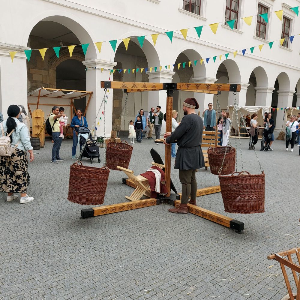 Ein mittelalterliches Kinderkarussell. Mit einem Mann, der es dreht und einem Kind in einem der Körbe. Mittelaltermarkt auf der Burg Hrad.