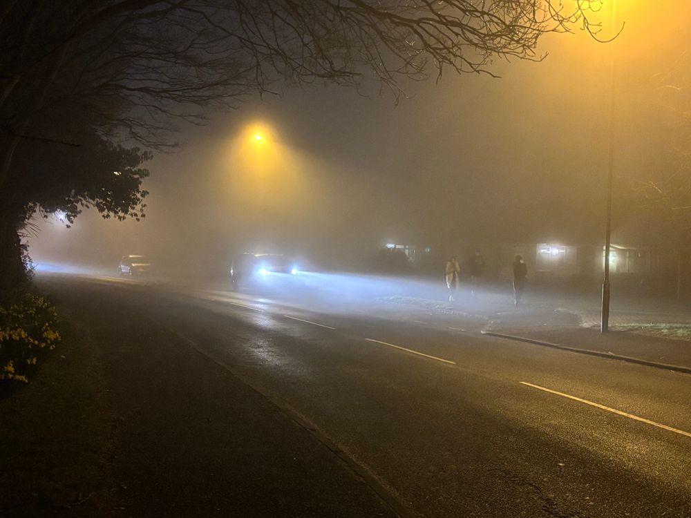 Foggy street with a stopped car that still has its lights on 