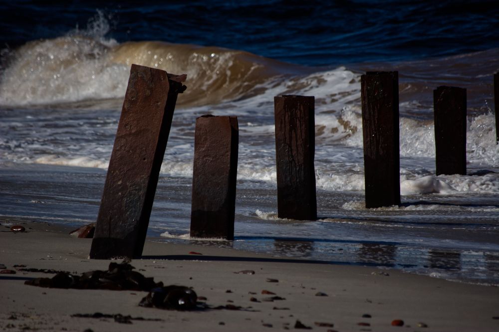 Strand und Brandung. Eine gleichmäßige Reihe rostiger Wellenbrechen ist mit weißen Schaumkronen und im Hintergrund einer Welle zu sehen. Das Wasser scheint sowohl blau als auch braun zu sein.