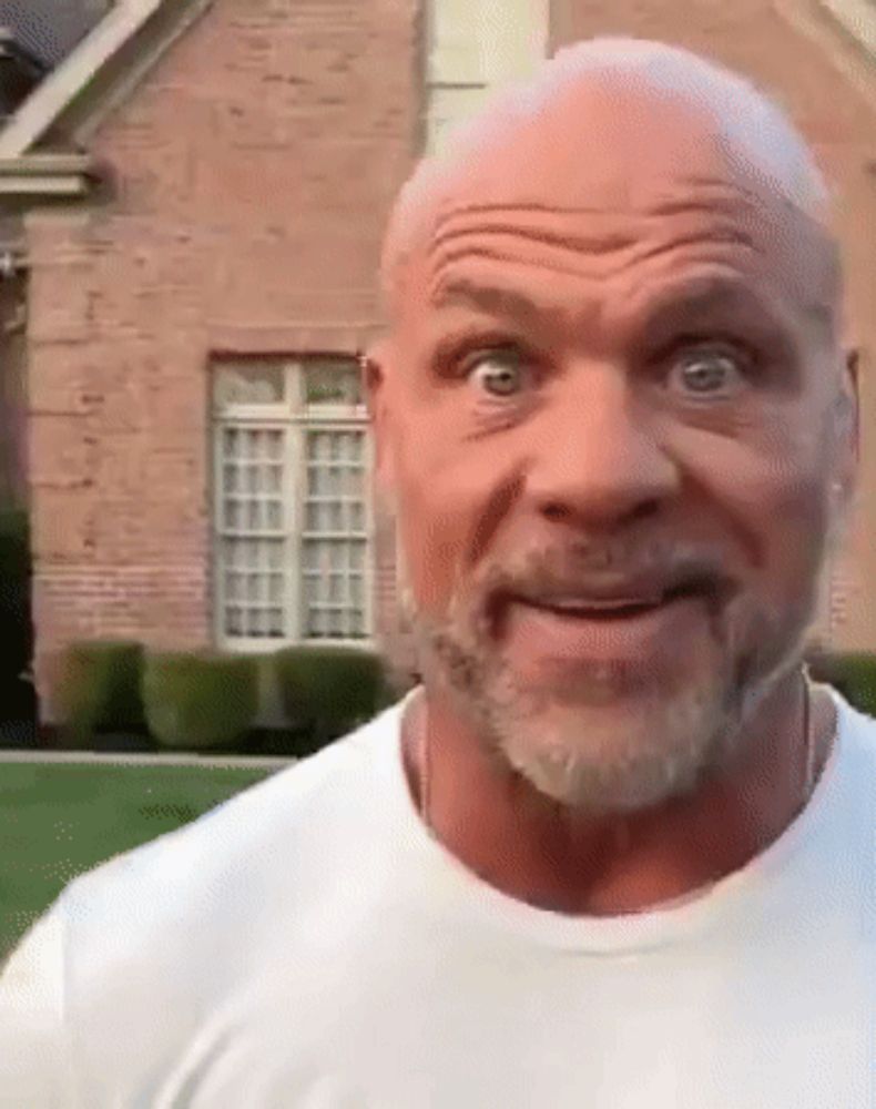 a bald man with a beard is making a funny face in front of a brick building