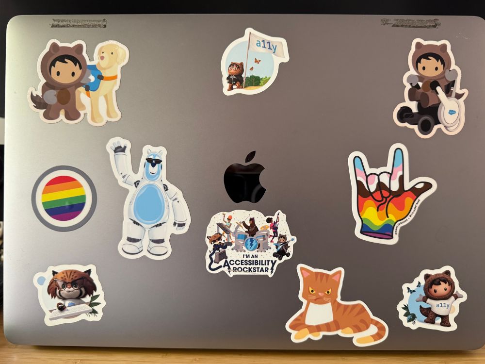 Mac laptop lid with stickers of Salesforce mascots, and accessibility and LGBTQ symbols