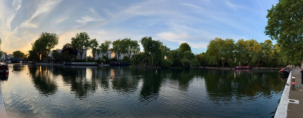 Canal at sunset with golden light reflecting on the water, flanked by white buildings and trees.