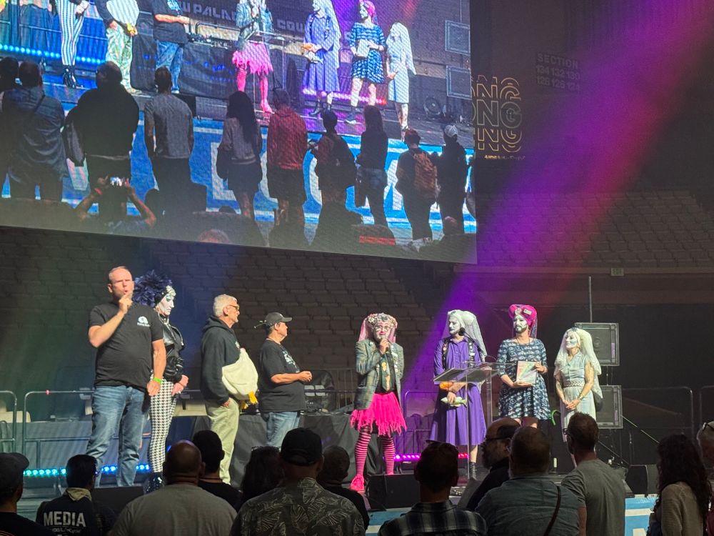 Stage with men dressed as nuns and a man wearing a large rubber chicken and an ASL interpreter. 