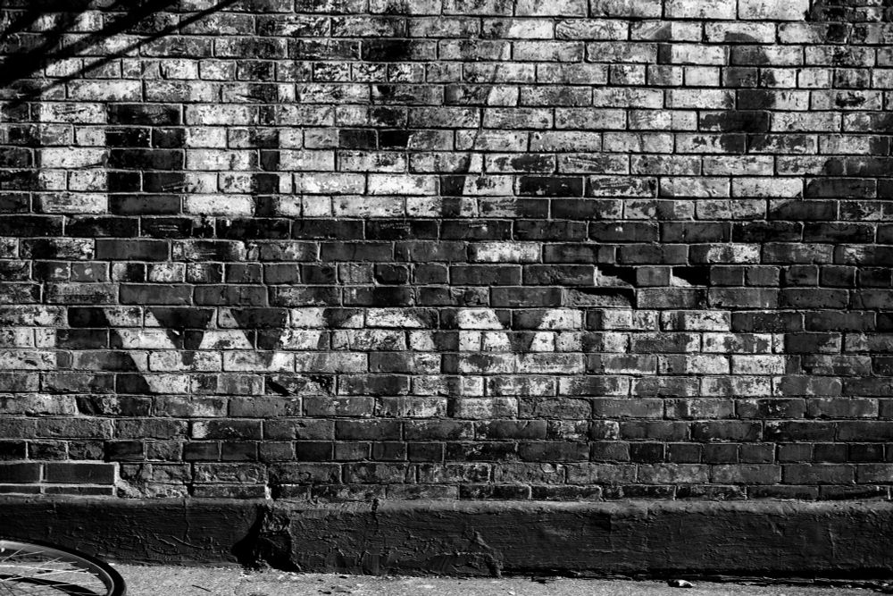 A black-and-white photo of a brick wall with part of a ghost logo. It reads "Head" and "Women". I've no idea what the entire logo said. 