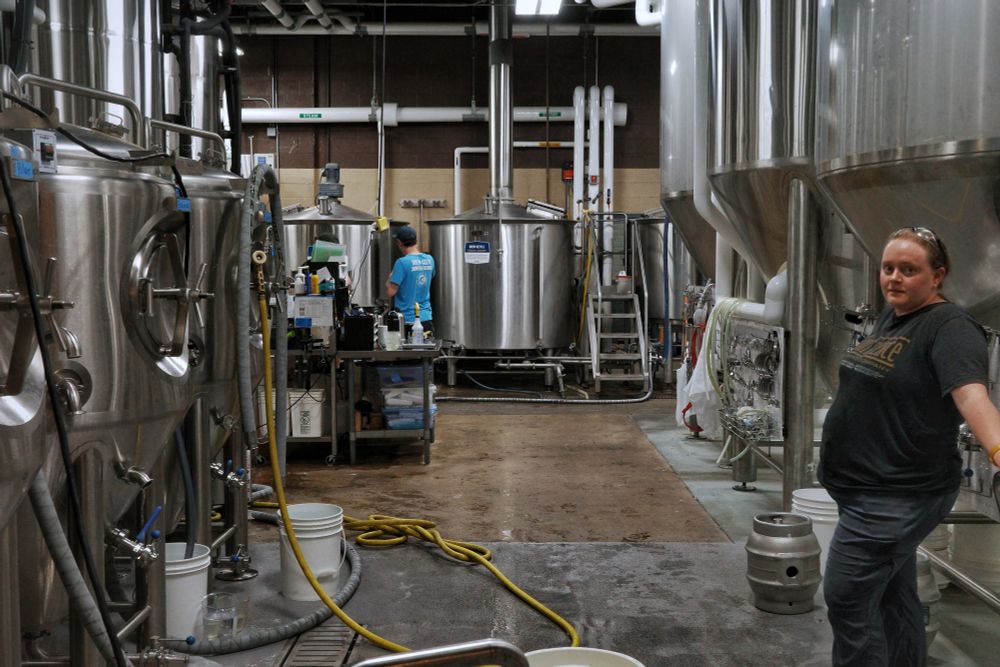 A peek into the beer brewing process. Large shiny metal vats attended by a young man and woman.