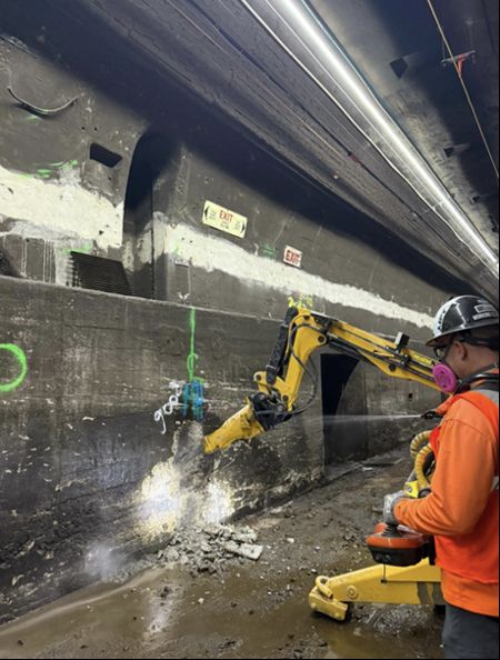 A tiny excavator demolishes part of a bench wall in a tunnel. Photo from Amtrak.