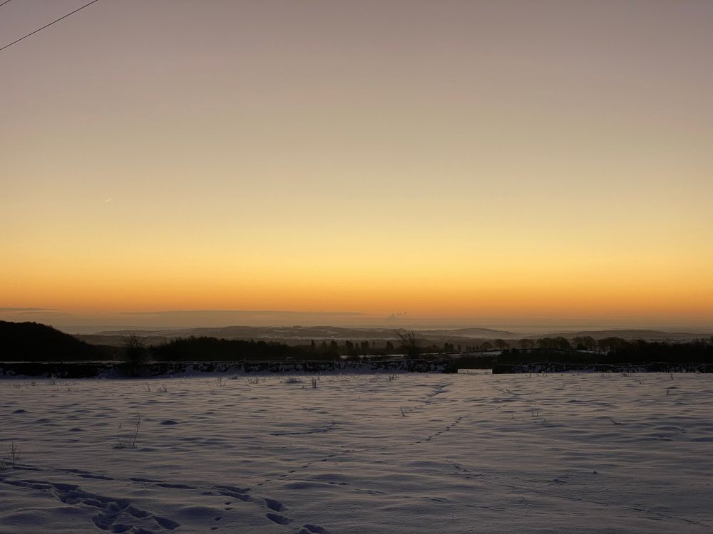 A photo of a snowy field with the glow of the sun about to rise around the horizon