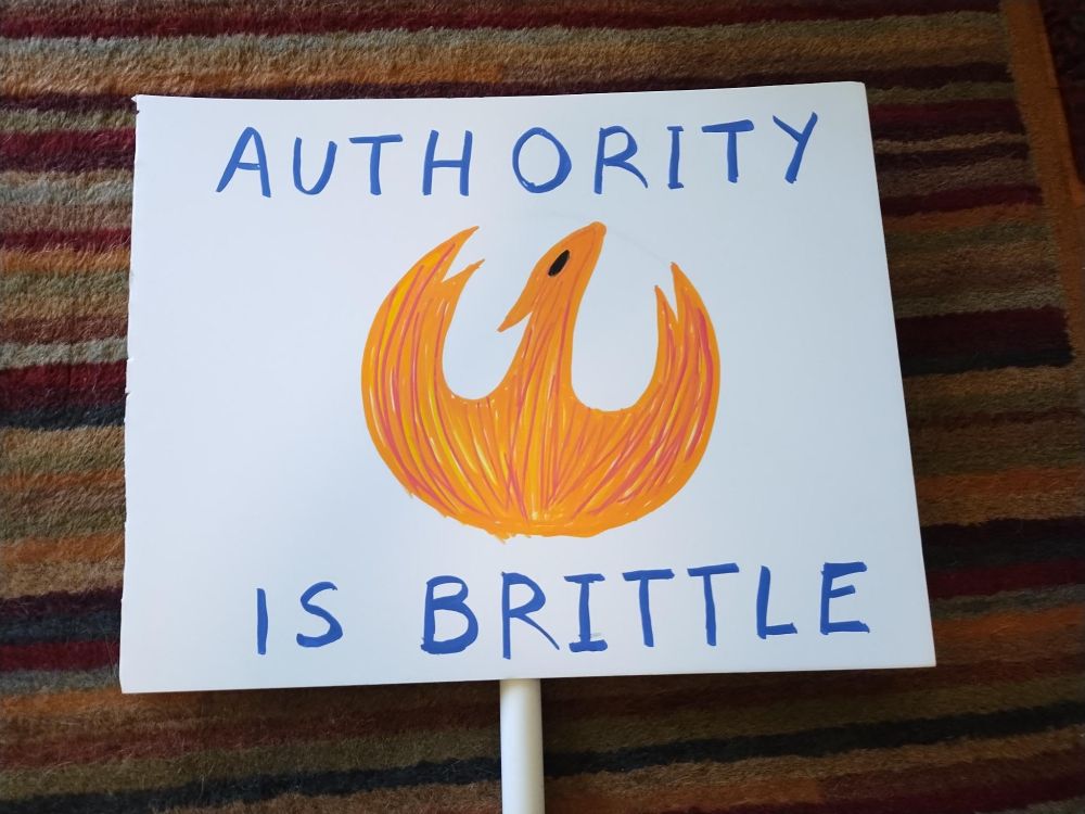 white foamboard sign that says "Authority is Brittle" above a Star Wars rebellion firebird