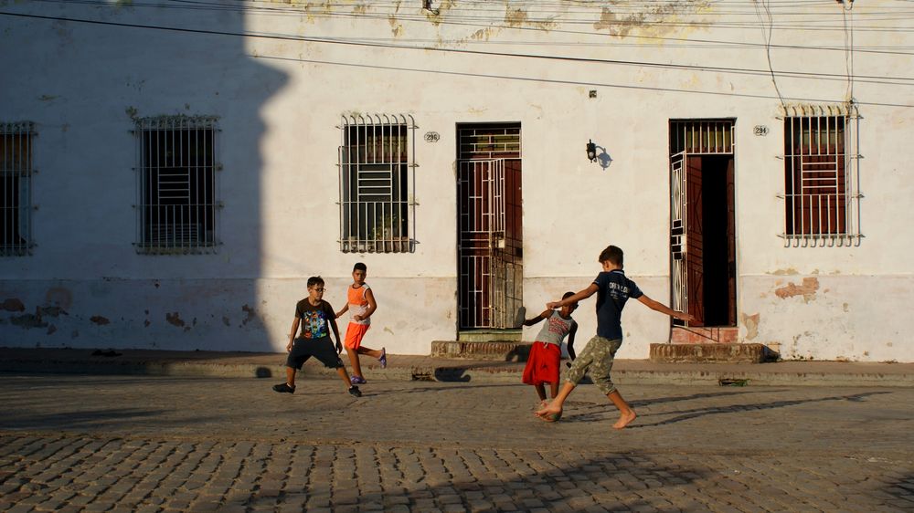 Kinder spielen auf der Straße Fußball, teils barfuß, teils mit Schuhen