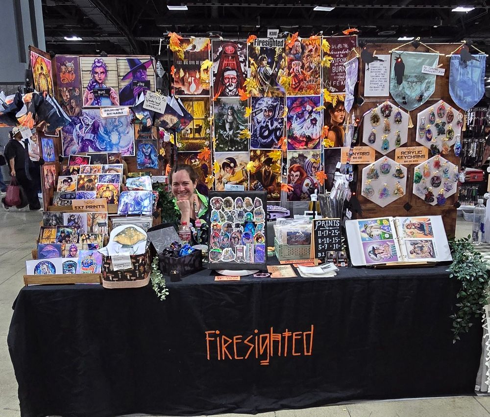 Photograph of my artist alley table at Otakon featuring art prints, bags, keychains, original work, and fanart.
