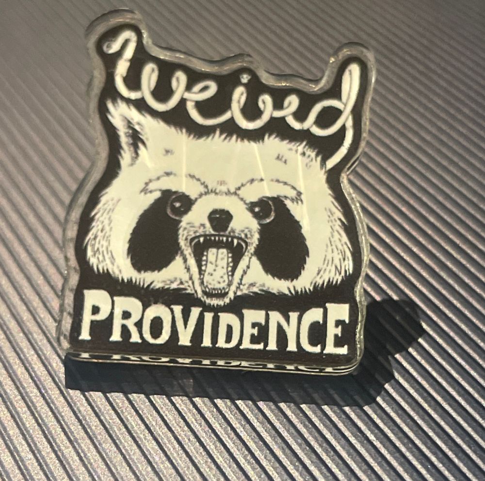 A pin featuring a screaming raccoon surrounded by the text WEIRD PROVIDENCE 