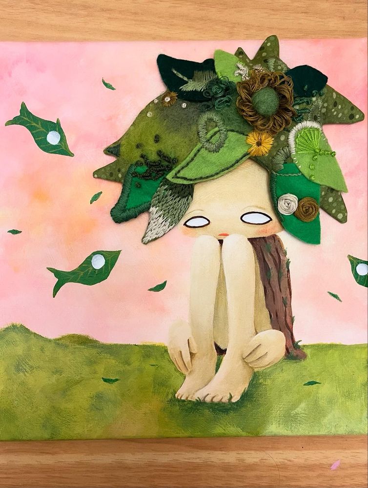 Mixed media painting on a canvas. A tree person sitting in the field with fish-leaves in the air. A tree person has leaves as hair, and the hair is done with embroidered fabric. 