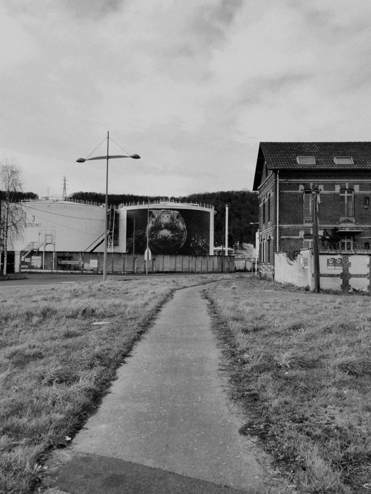 Photo noir et blanc d'une maison isolée au milieu de grand réservoir de stockage (de pétrole peut-être). Sentiment âpre de zone industriel sans dimension humaine. 