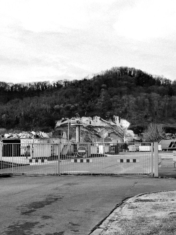 Photo noir et blanc d'une route avec une grille fermé sur une zone industrielle d'entrepôts. 