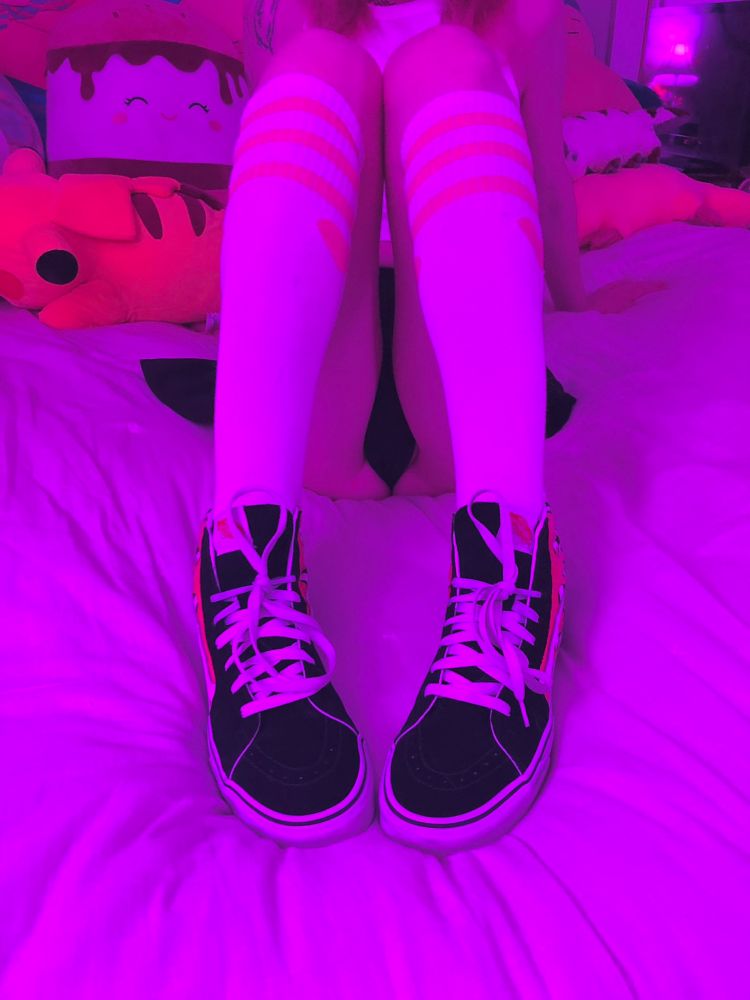Photo of me sitting in bed, leaning back with my knees up. I'm wearing Vans high-top sneakers and knee high striped athletic socks with hearts on them. My black panties and black skater skirt are just barely visible behind and in-between my legs.