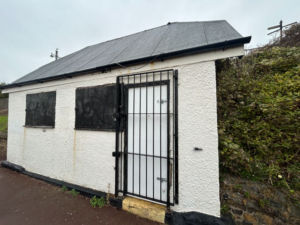 Boarded up small pebbledash hut with gated door on Clacton seafront.