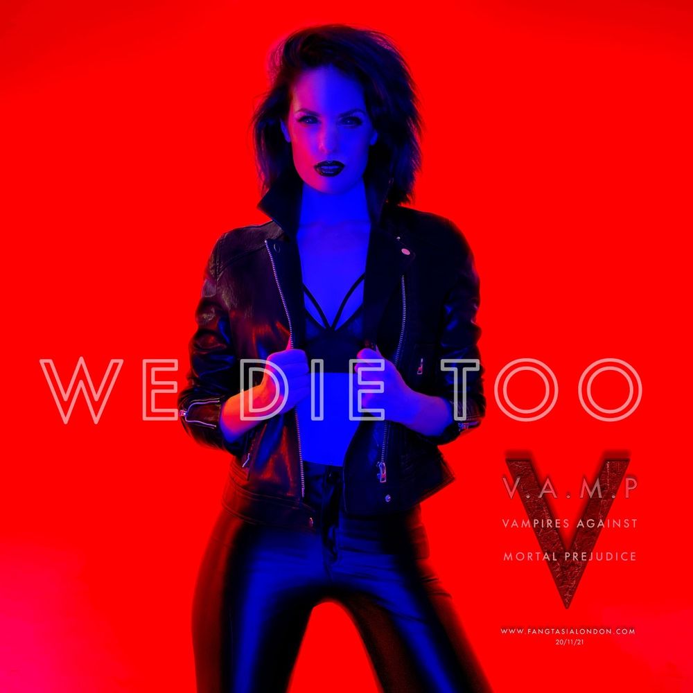 Photo taken in 2021 of Sarah a 30 something white woman in black lycra leggings and a leather jacket posing as a vampire in front of a red backdrop for vampire themed night club promotion material 