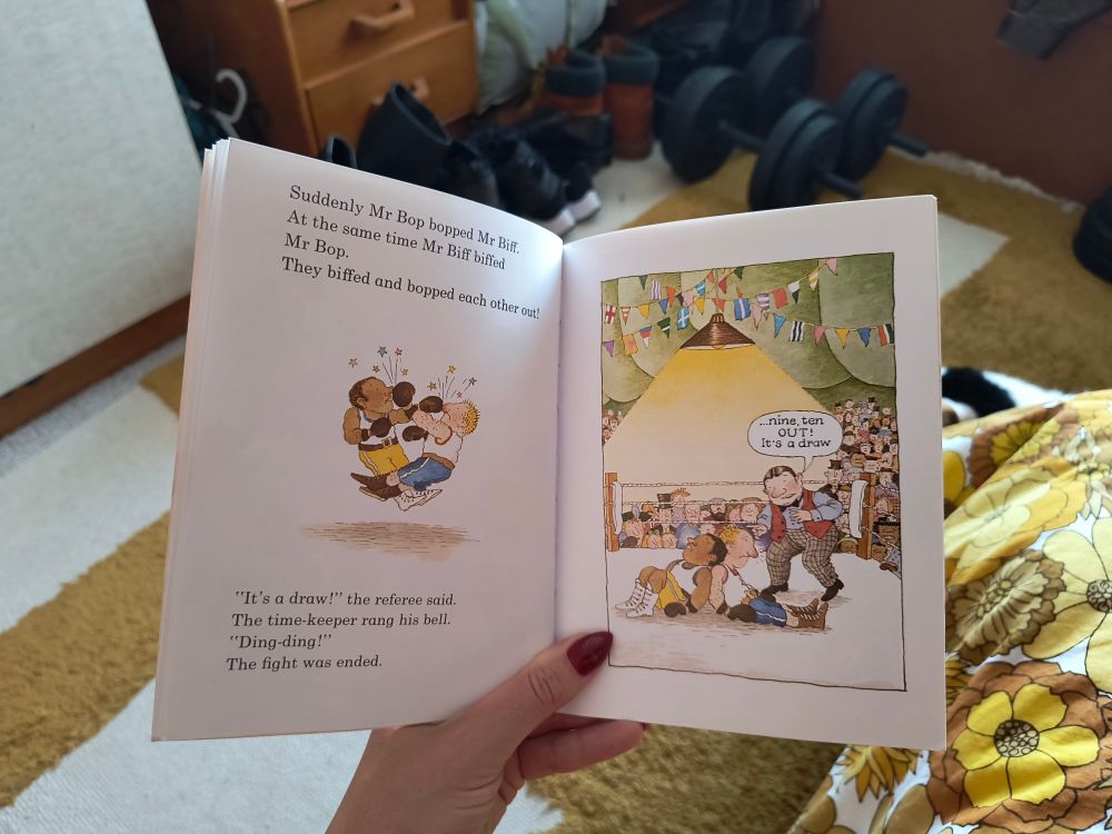 Photo of an action scene from the 1980 book Mr Biff the Boxer. Illustration  shows two boxers collapsed on the floor of a ring. Text reads Suddenly Mr Bop bopped Mr Biff at the same time Mr Biff biffed Mr Bop. They biffed and bopped each other out! It's a draw the referee said. The timekeeper rang his bell. The fight was ended.