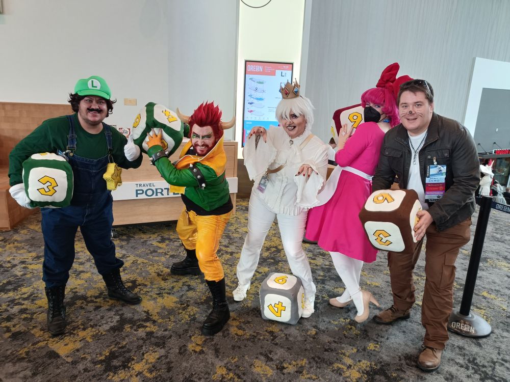 A Mario Party cosplay group featuring Luigi with human versions of Bowser, King Boo, Birdo, and Monty Mole, holding large plush dice