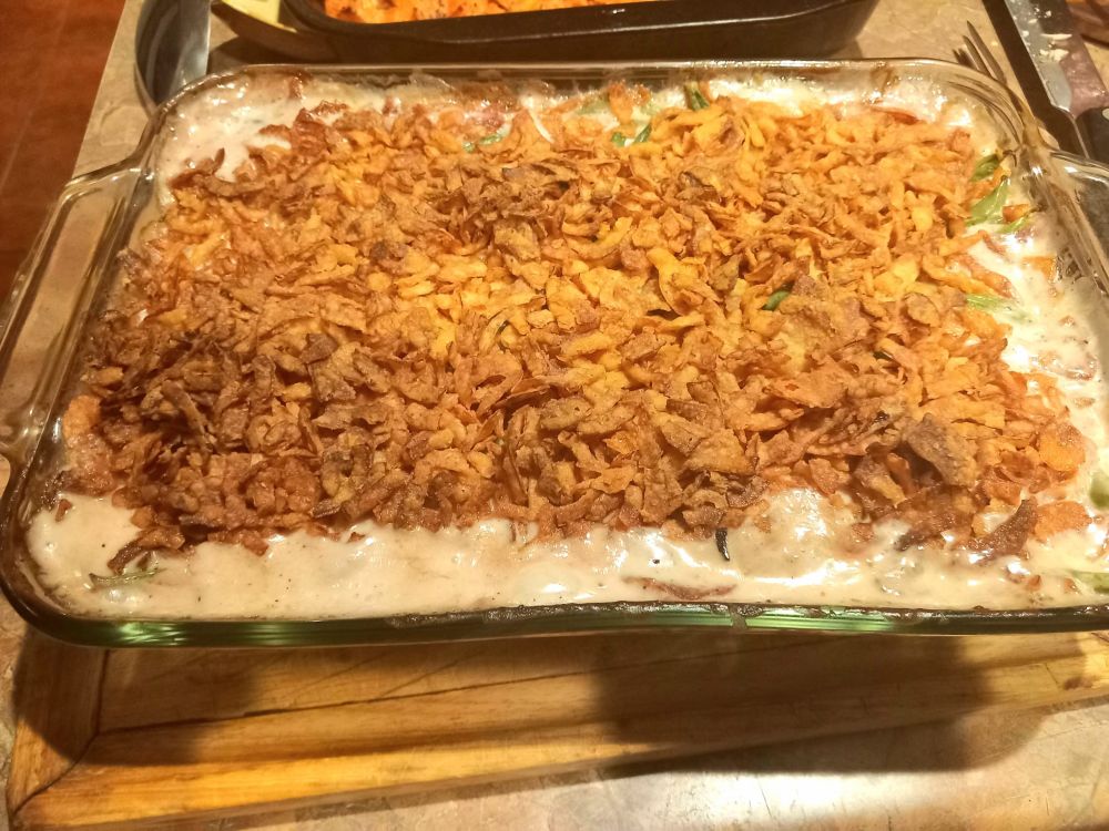 A glass baking dish of green bean casserole, covered in crispy onions. The mushroom cream sauce is bubbling up on all sides