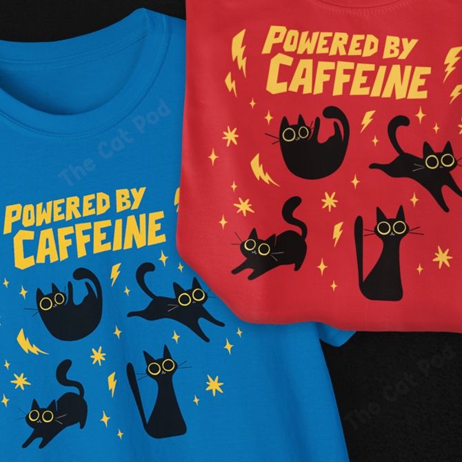 Two t-shirts, one red and one blue, depicting four energetic black cats with big dilated eyes and yellow sparks around them. The text above says "powered by caffeine". 