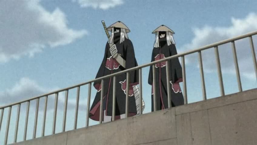 Duas pessoas usando trajes semelhantes, mantos pretos com estampas de nuvens vermelhas. O da esquerda porta uma espada nas costas, ambos de chapéu, cobrindo seus rostos com sombra. Estão no alto de um muro, atrás de grades.