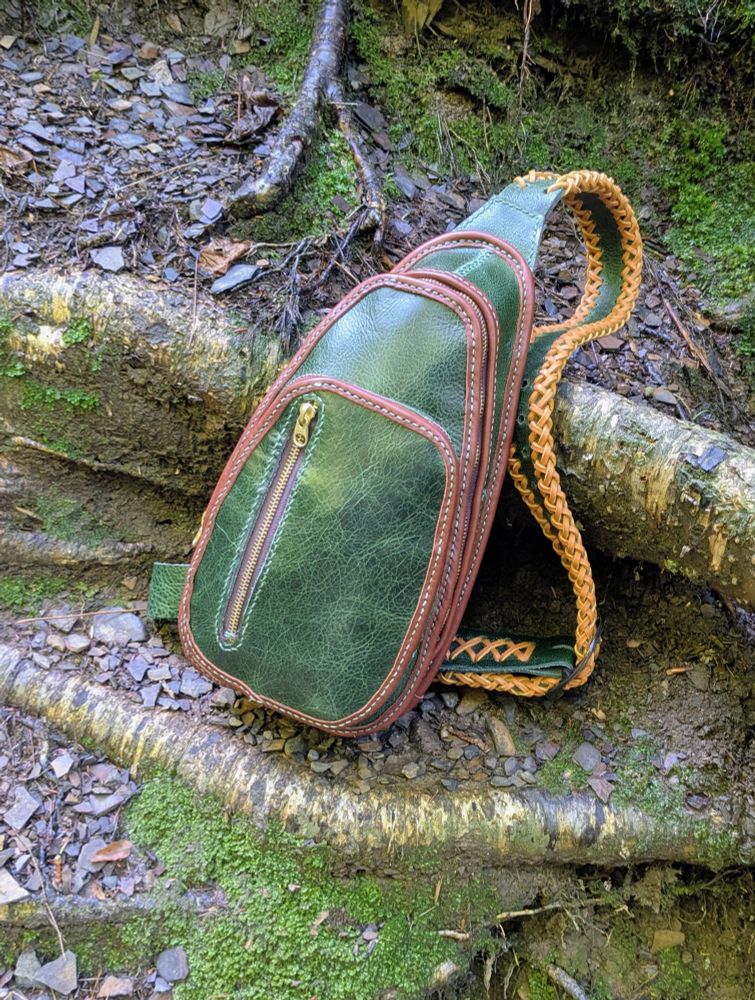 Picture of a green and brown leather sling style crossbody bag.