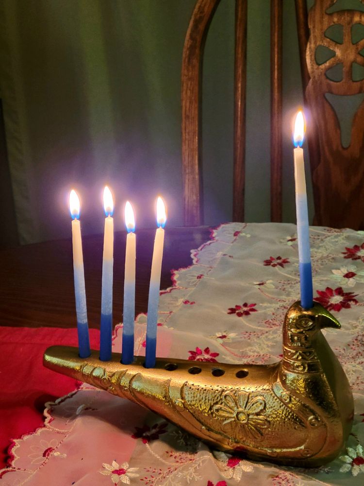 Gold dove-shaped menorah with 4 candles and one servant candle sits on a table covered with a red-and-white lace runner and red placemats.