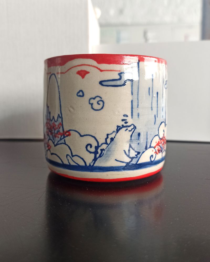 Close shot of the ceramic cup, the small Godzilla in bathing in hot springs
Blue underglaze lineart with watercolor effects, Red underglaze patterns and details (cherry blossom dots)