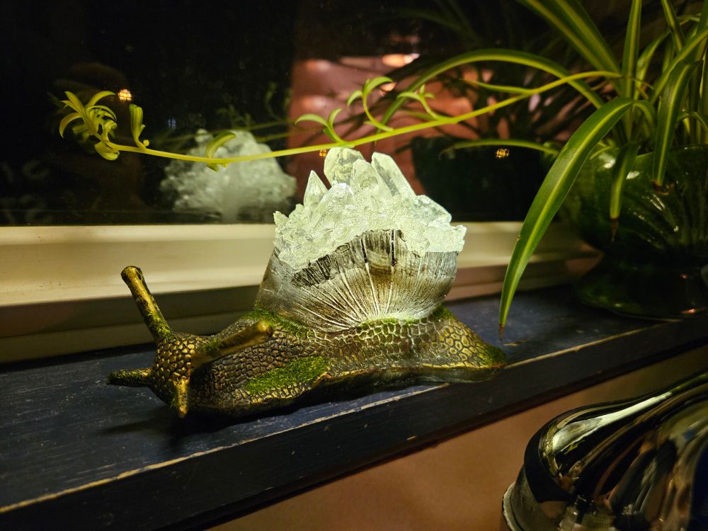A resin cast snail sculpture with a crystal effect on the shell that illuminates from within. In this picture there is more light showing the gold and green details on the slug's body.