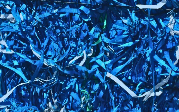 A dense pile of shredded blue plastic strips mixed with a few white and green pieces, creating a tangled, textured pattern.