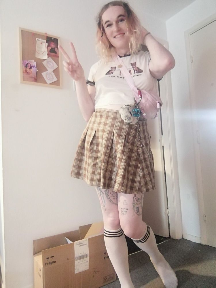 Sophie is standing in her living room a little jauntily making a peace sign with her right hand, touching her hair with her left and giving you a big gorgeous grin. Her curls are big and bouncy today and with her wide grin she looks even more like a big cat who somehow was turned into a girl than usual. You think about her being a big cat. You think about her eating you. Your tummy tenses. She is wearing a plaid skirt, knee high socks, her pink bumbag and a t shirt with a lacey collar.