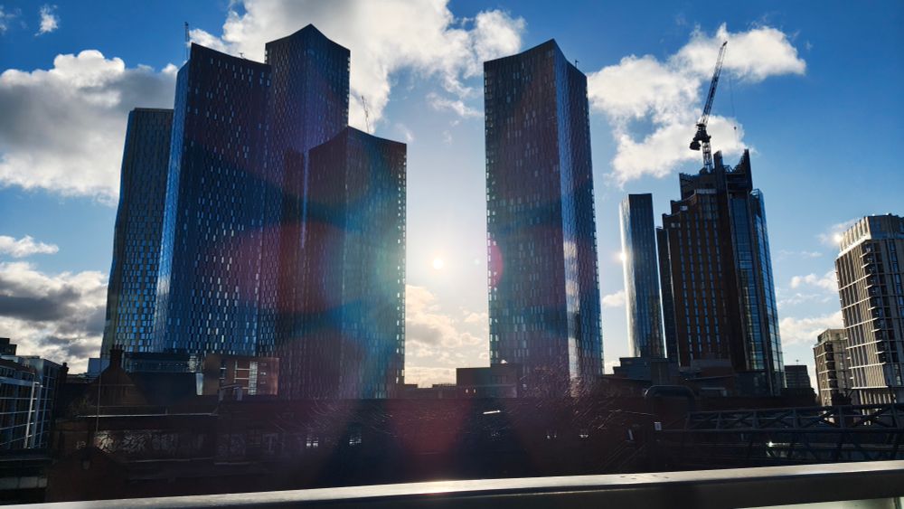 Photo of the Manchester skyline with the sun shining through between two buildings 