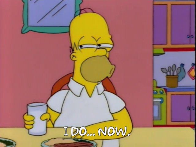 Homer sitting at the dinner table with a glass of milk. He's doing a squinty side eye and saying "I do... now."