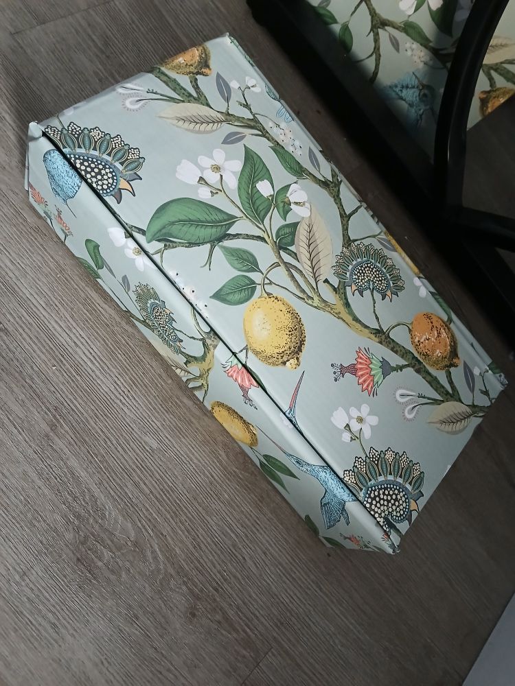 A closed cardboard box full of craft shit BUT IT HAS BEEN TURNED INTO A VINTAGE DELIGHT THROUGH THE MAGIC OF PEEL AND STICK WALLPAPER 