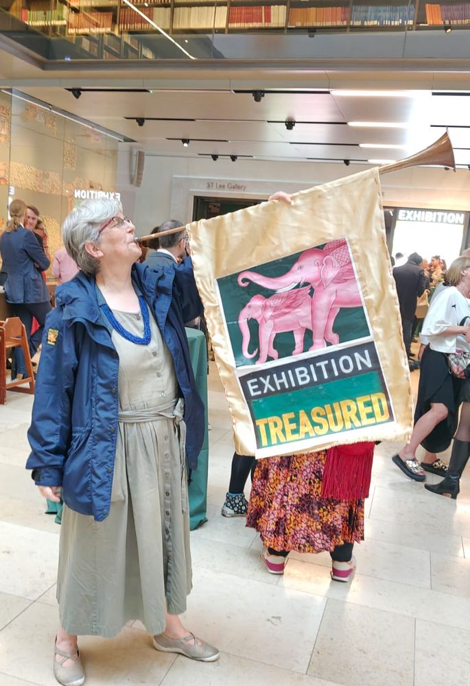 Woman blowing a hunting horn with a banner showing two pink elephants and the caption 'Exhibition Treasured'