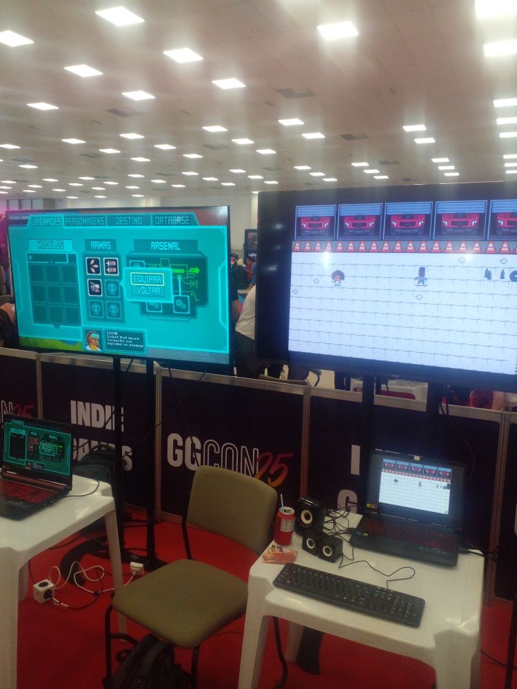 Dois notebooks em cima de mesas de plastico cada um conectado a um telao mostrando os jogos railgunners e skaterpg