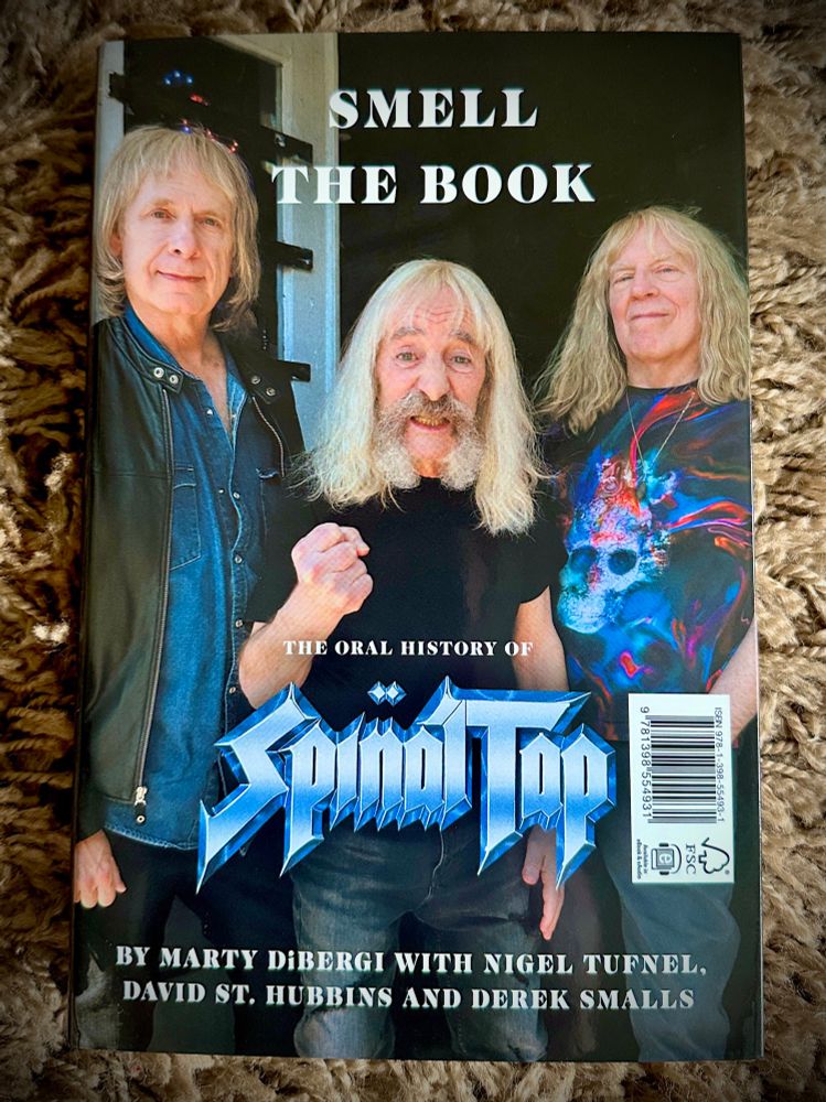 Back cover of the same book, titled Smell the Book: The Oral History of Spinal Tap. It shows three older band members smiling and posing together, wearing casual clothing.
