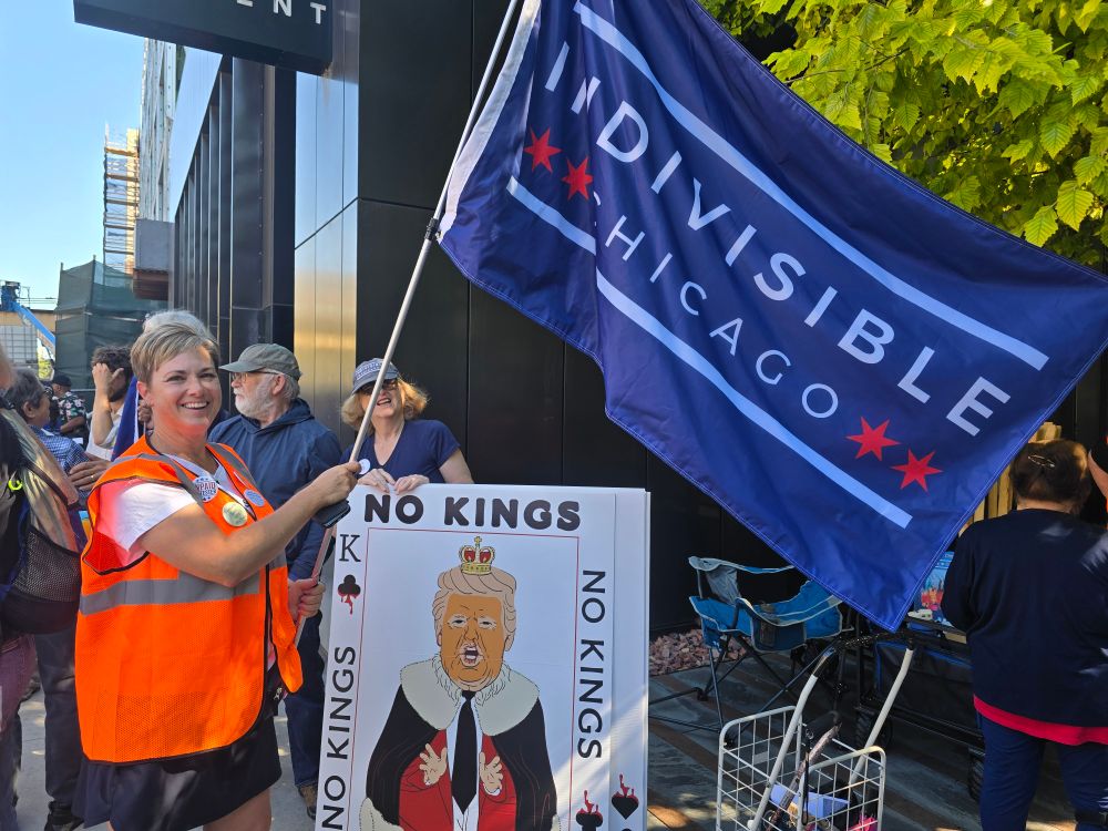 Volunteer in orange vest holds Indivisible Chicago flag and a sign saying no kings 